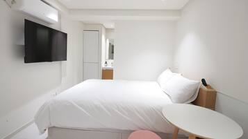 A modern hotel room with a bed, a small round table, a television mounted on the wall, and a mirror.