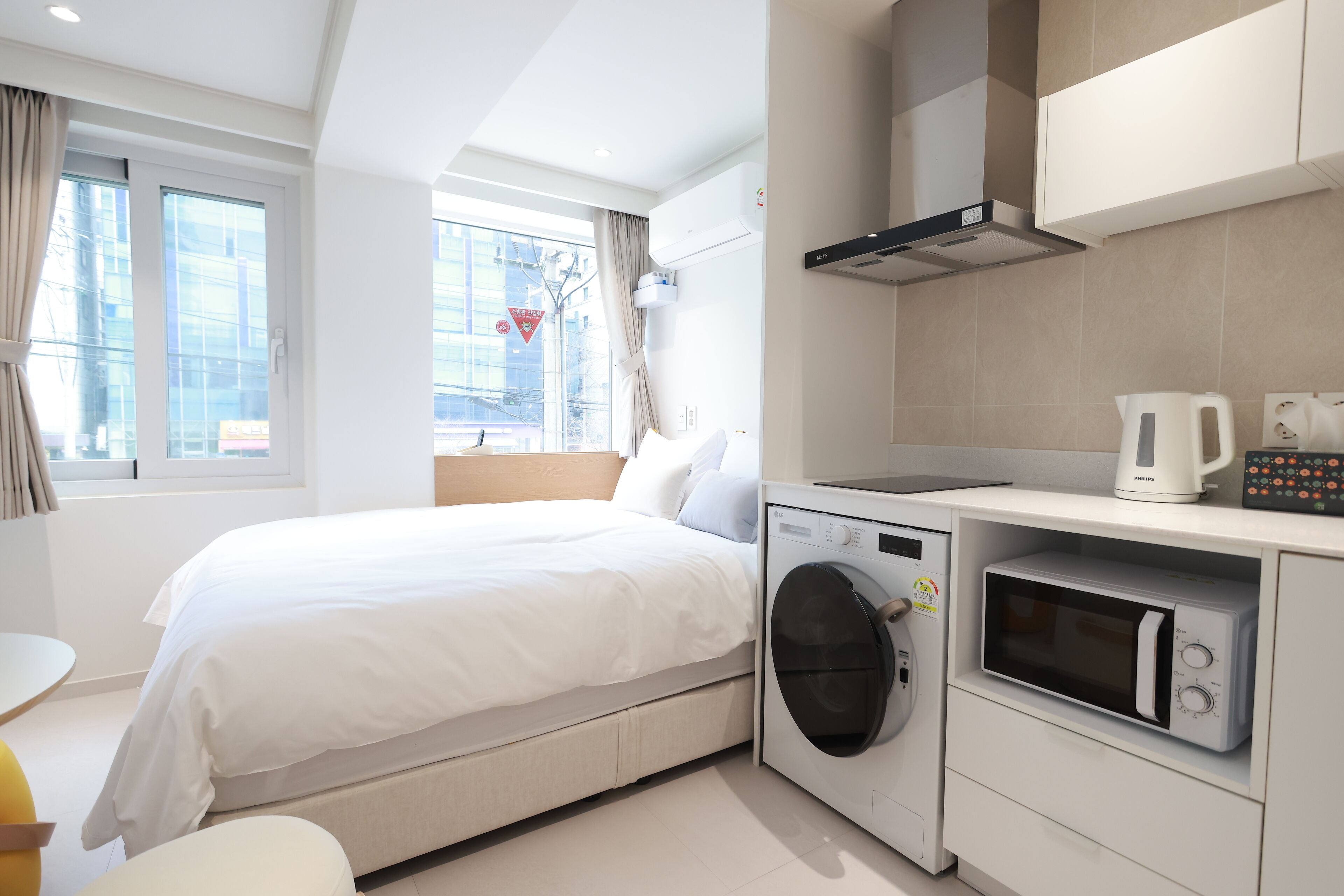Una habitación de hotel moderna con cama, lavadora, microondas y vista a la ciudad.
