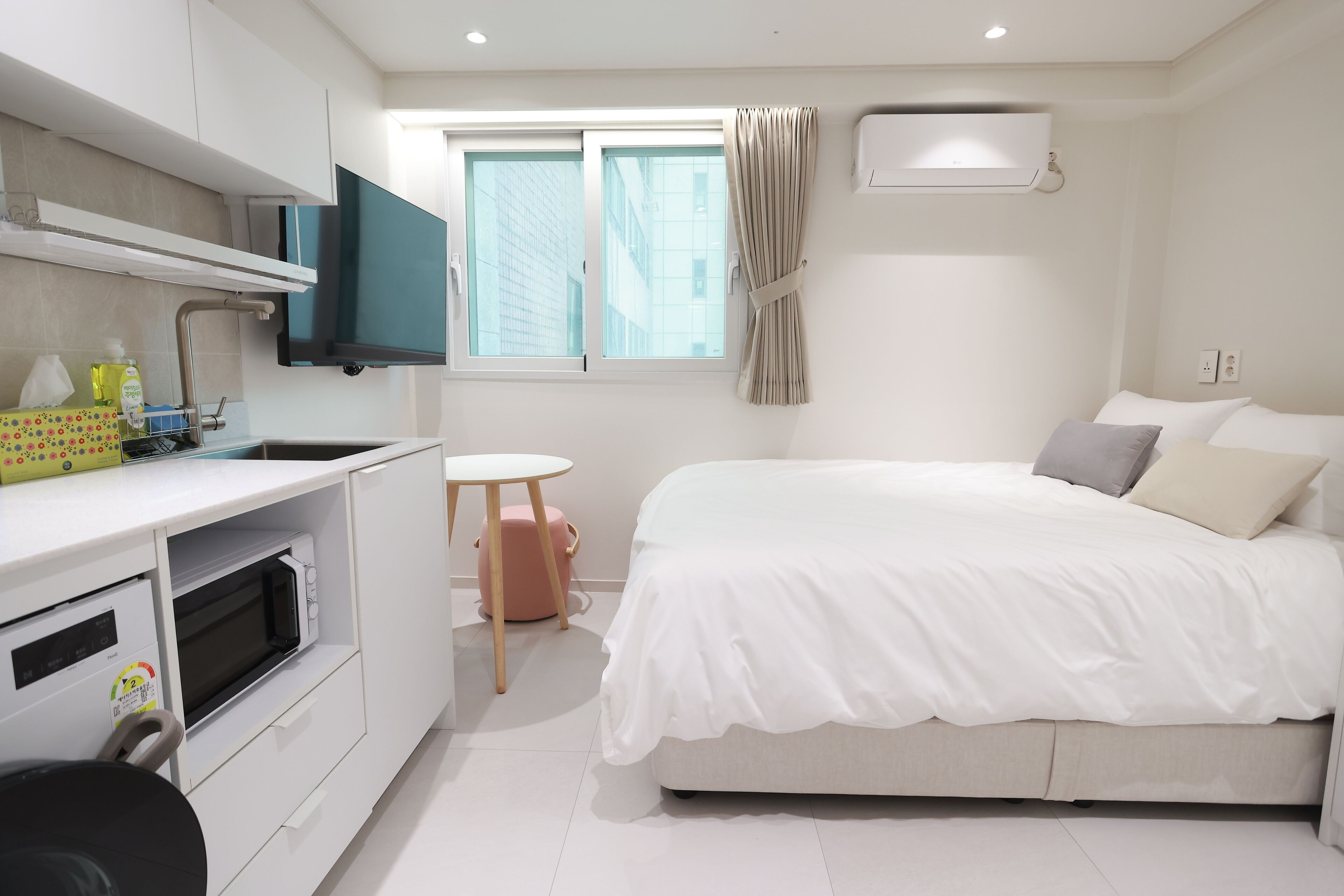 A modern bedroom with a bed, a small table, a microwave, and a window with curtains.