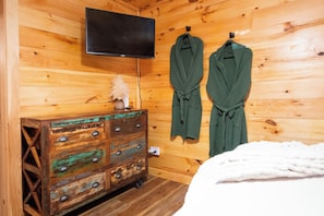 Una habitación de madera con una televisión, un aparador de madera y dos albornoces verdes colgados en la pared.