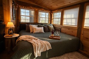 A cozy cabin room with a bed, a lamp, a tray with a bottle and glasses, and a blanket. - Whiskey N Wine Ridge: Fire Pit, Hot Tub, Ample Parking, pets, near Pigeon Forge (Sevierville)