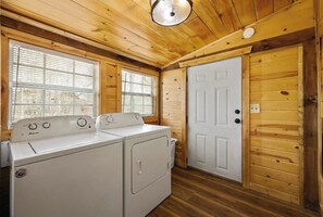 A laundry room with two washing machines, wooden walls, a white door, and windows with blinds. - Whiskey N Wine Ridge: Fire Pit, Hot Tub, Ample Parking, pets, near Pigeon Forge (Sevierville)