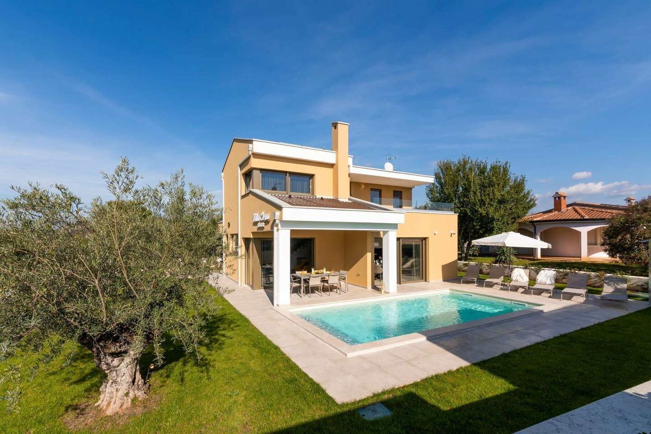 Una casa moderna de dos pisos con piscina, mobiliario exterior y un césped bien cuidado.