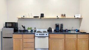 A kitchen with a stove, microwave, refrigerator, wooden cabinets, and a coffee maker. - Historic Harmar Studio | Walk to Dining (494751) (Marietta)