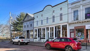 A street with a red car parked on the side, a white truck, and a building with a large window and a mural on the side. - Historic Harmar Studio | Walk to Dining (494751) (Marietta)