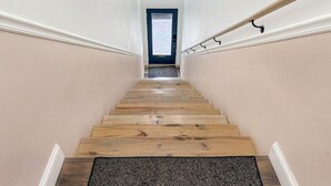 A wooden staircase with a blue door at the top, white walls, and a handrail on the right. - Historic Harmar Studio | Walk to Dining (494751) (Marietta)