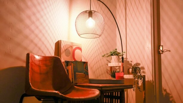 Et værelse med en læderstol, et bord med bøger og en lampe, samt en lampe monteret på væggen.