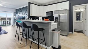 A modern kitchen with white cabinets, a stainless steel refrigerator, a microwave, and a bar area with stools.