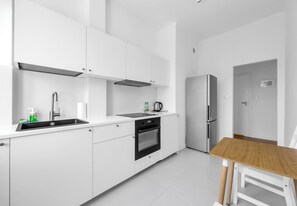 Eine moderne Küche mit weißen Schränken, einer Edelstahl-Spüle, einem eingebauten Backofen und einem Kühlschrank.