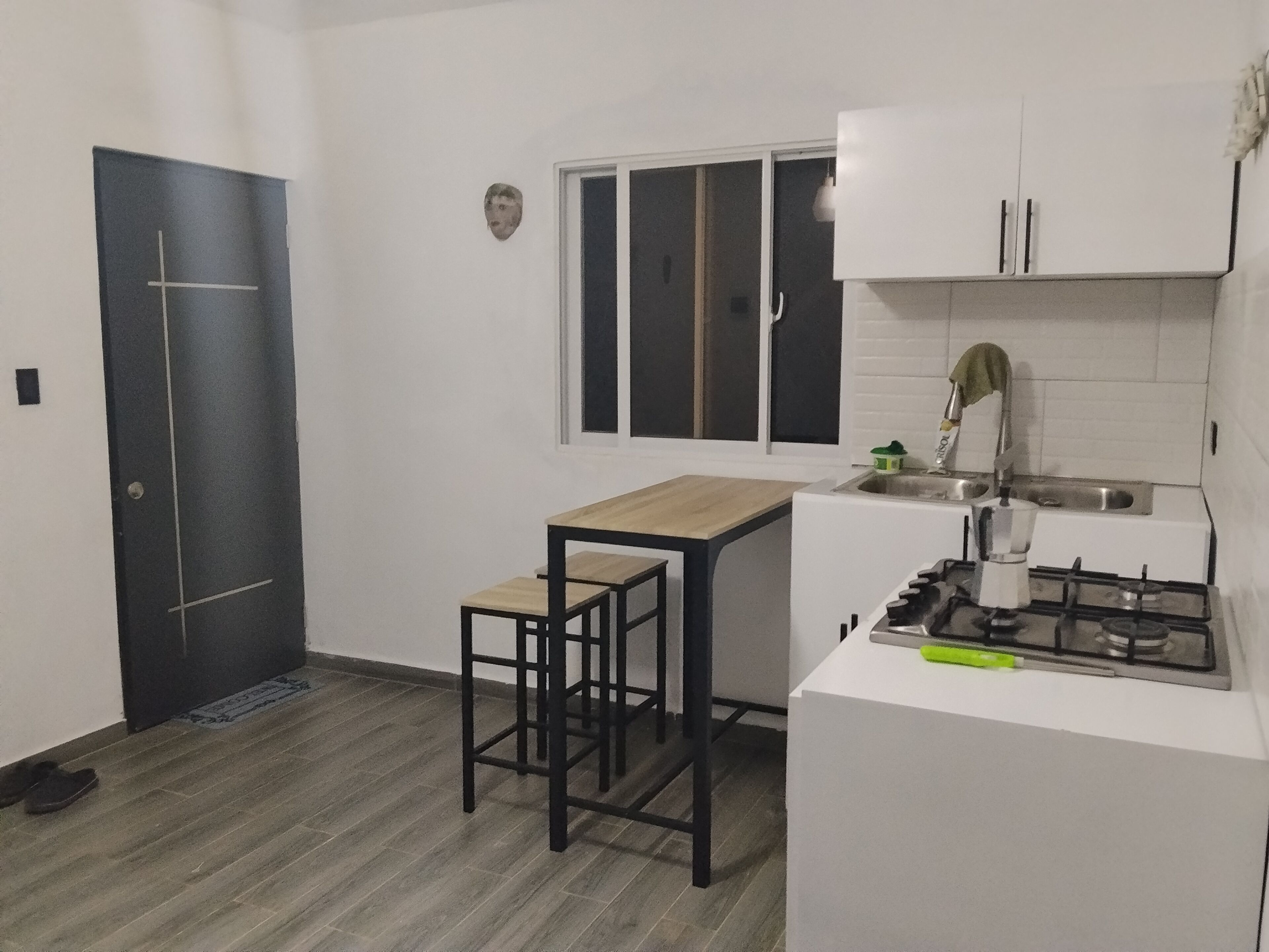A compact kitchen with a dark door, a small window, a white countertop, a gas stove, and a sink.