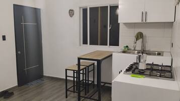 A compact kitchen with a dark door, a small window, a white countertop, a gas stove, and a sink.
