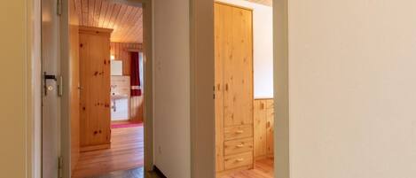 Ein Korridor mit Holzboden und -wänden, der zu einem Raum mit Holzschrank und Fenster führt.