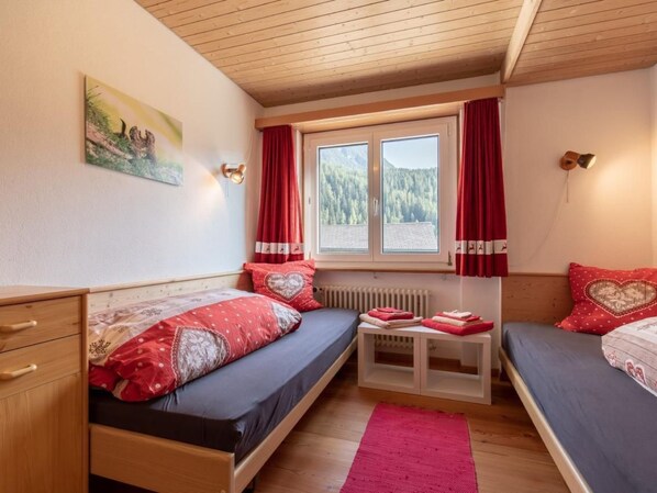 Et hyggeligt værelse med to senge, et lille bord, en radiator og et vindue med gardiner.