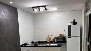 Una cucina moderna con zona pranzo, che include un tavolo in legno, sedie in vimini, un’isola integrata e un frigorifero bianco.