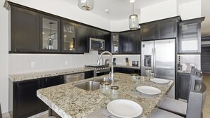 Eine moderne Küche mit dunklen Schränken, Granit Arbeitsplatten, Edelstahlgeräten und einer zentralen Kochinsel mit Sitzgelegenheiten.