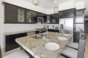 A modern kitchen with dark cabinetry, granite countertops, stainless steel appliances, and a central island with seating. - 1452  Ocean Front 2 bedroom (Bajos de Chila)
