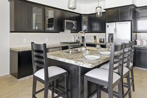 A modern kitchen with dark cabinetry, granite countertops, a central island with seating, stainless steel appliances, and pendant lighting. - 1452  Ocean Front 2 bedroom (Bajos de Chila)