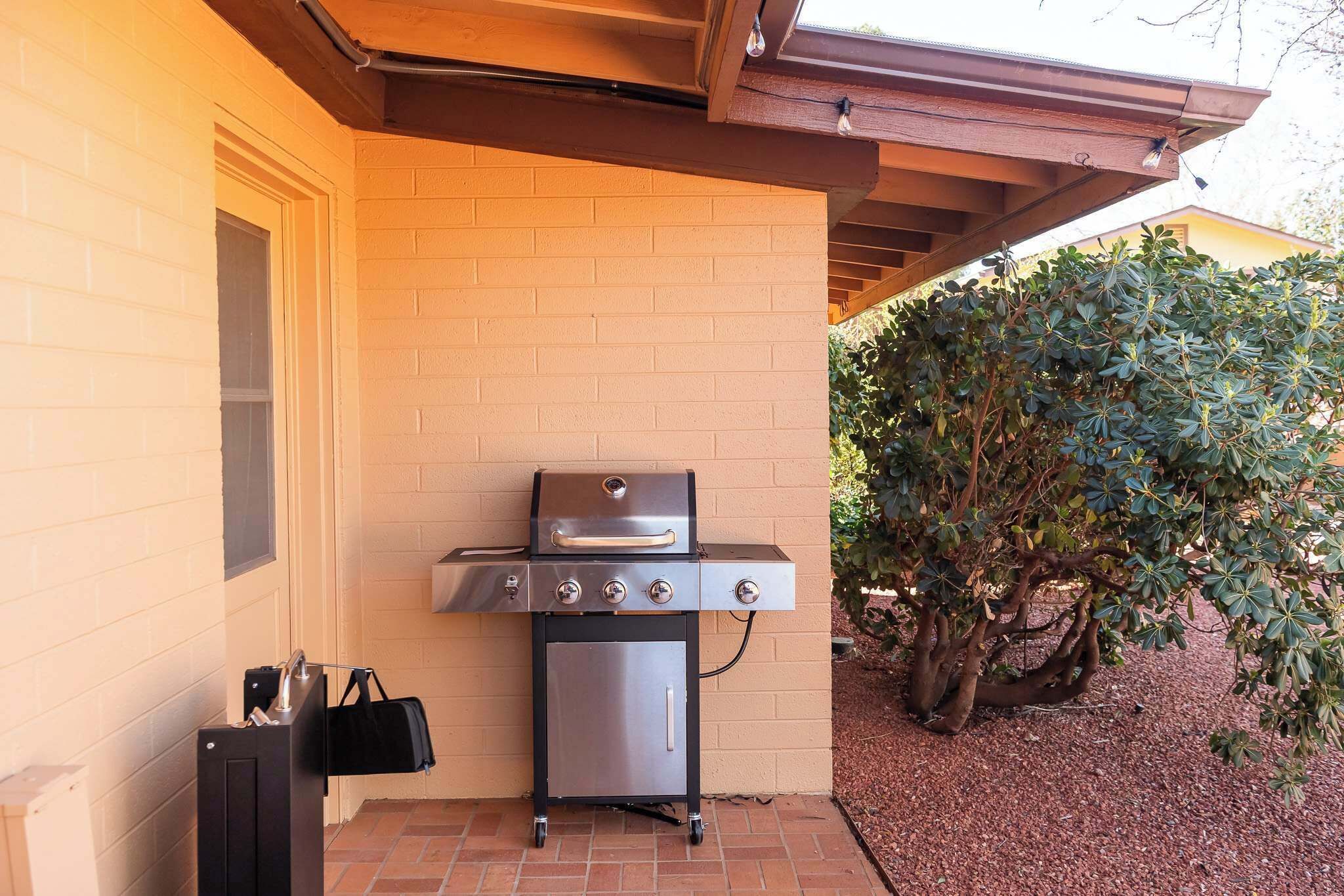 A portable grill on a brick patio with a brick wall and a tree in the background.