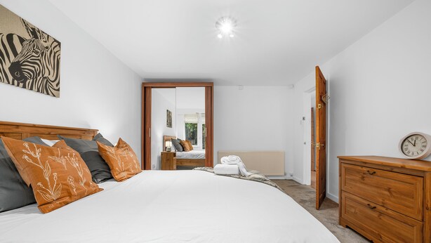 Een slaapkamer met een groot bed, een houten dressoir, een spiegel en een deur naar een andere kamer.