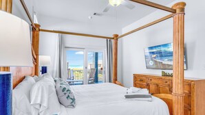 Ein Bett mit Baldachin mit Blick auf das Meer, eine hölzerne Kommode und ein Fernseher an der Wand.