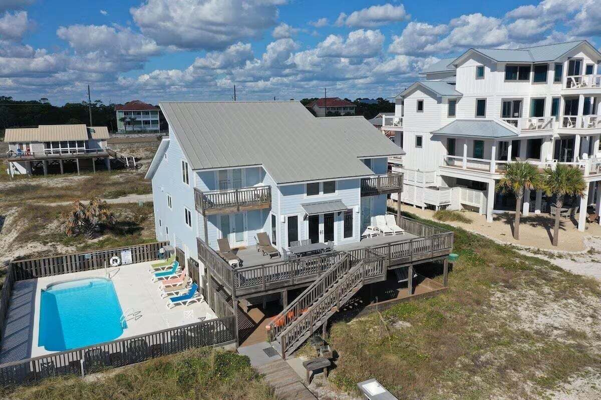 A beachfront property with a swimming pool, multiple decks, and a large house with balconies.