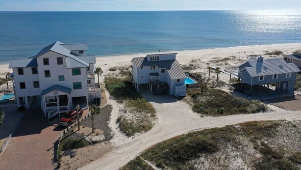 Una propiedad frente a la playa con varias construcciones, incluyendo un hotel grande con piscina y una casa más pequeña.