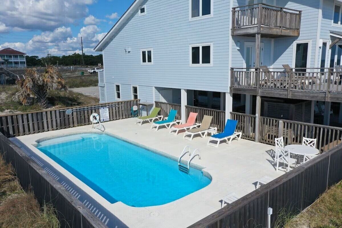 A pool area with a rectangular pool, lounge chairs, and a wooden deck.