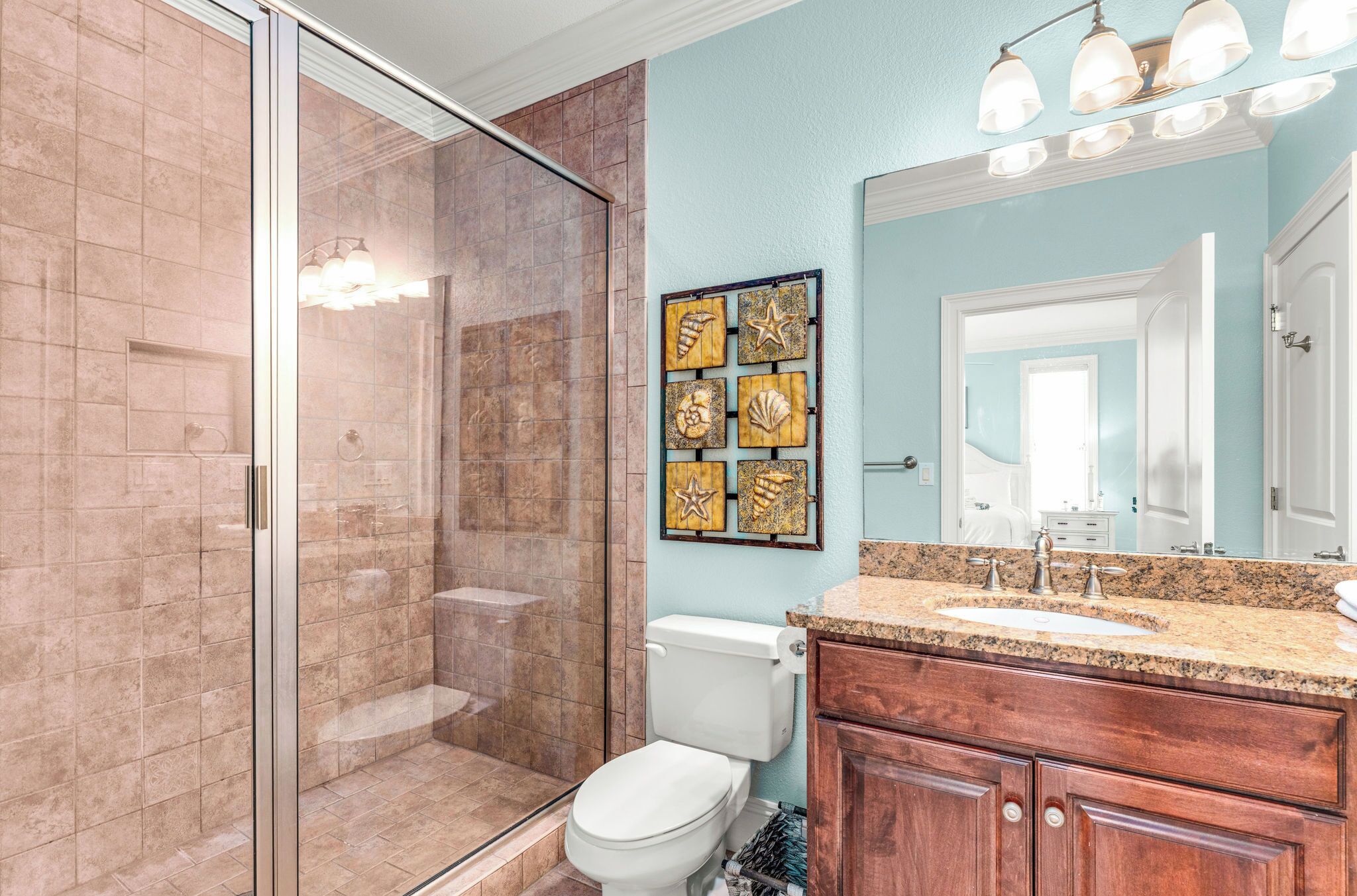 A bathroom with a glass shower enclosure, a white toilet, a vanity with a sink, and a mirror.