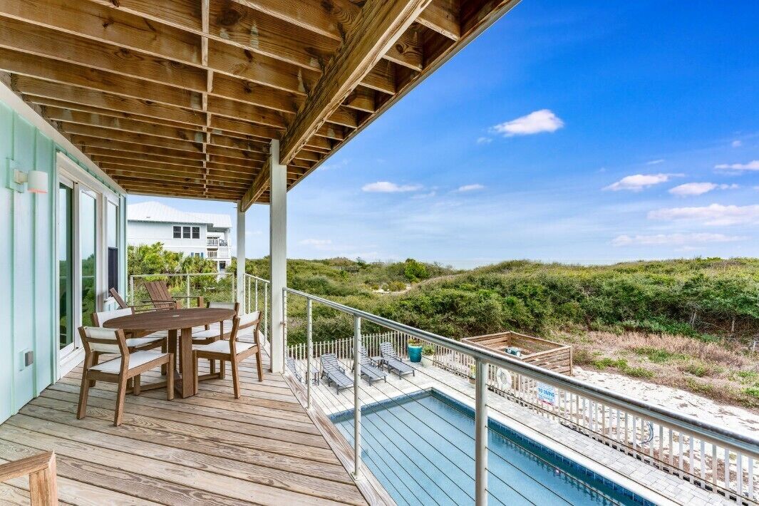 A wooden deck with a pool, outdoor seating, and a view of the beach.