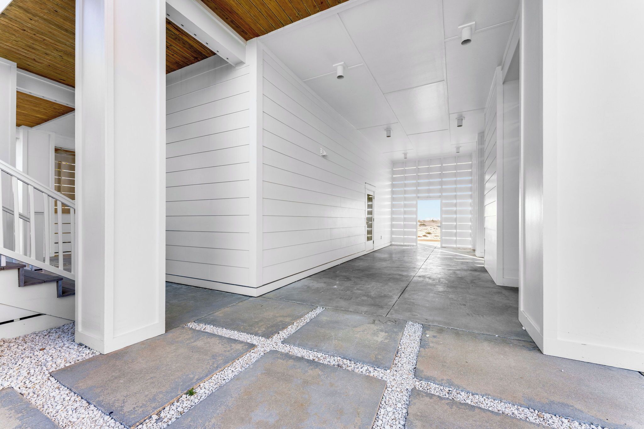 Un couloir aux murs blancs, au plafond en bois et au sol en béton agrémenté d’éléments en pierre.