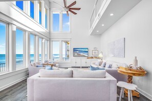 A spacious living room with large windows, a ceiling fan, and a view of the ocean. - Isle Dream - a premier beachfront retreat in the gated Plantation community! (St. George Island)