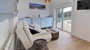 Ein großzügiger Wohnbereich mit einem weißen Sofa, einem Holztisch, einem rustikalen Fass, einem blauen Schrank und einem großen Fenster mit Blick ins Freie.