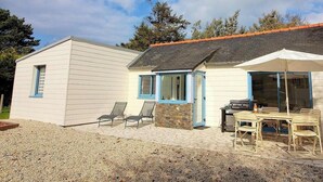 Ein kleines Haus mit Terrasse, Grill und zwei Stühlen.