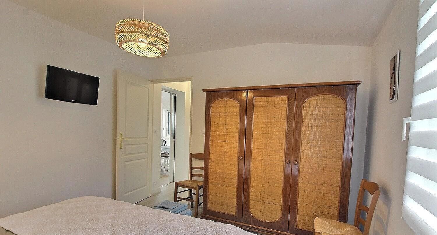 Une chambre à coucher comprenant un lit, une armoire, une chaise, un téléviseur et un luminaire suspendu.