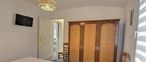 Une chambre à coucher comprenant un lit, une armoire, une chaise, un téléviseur et un luminaire suspendu.