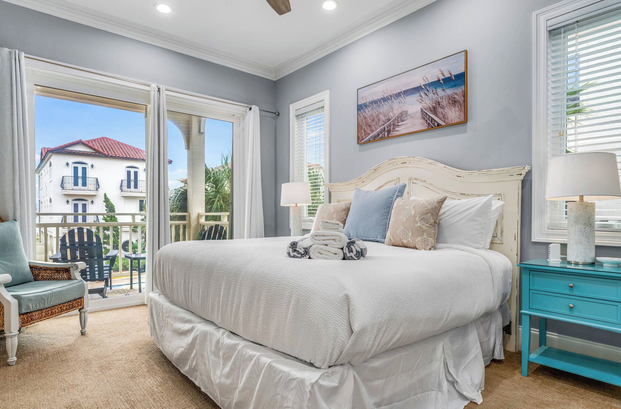 Quarto com cama grande, mesa de cabeceira, cadeira e varanda com vista para um edifício.