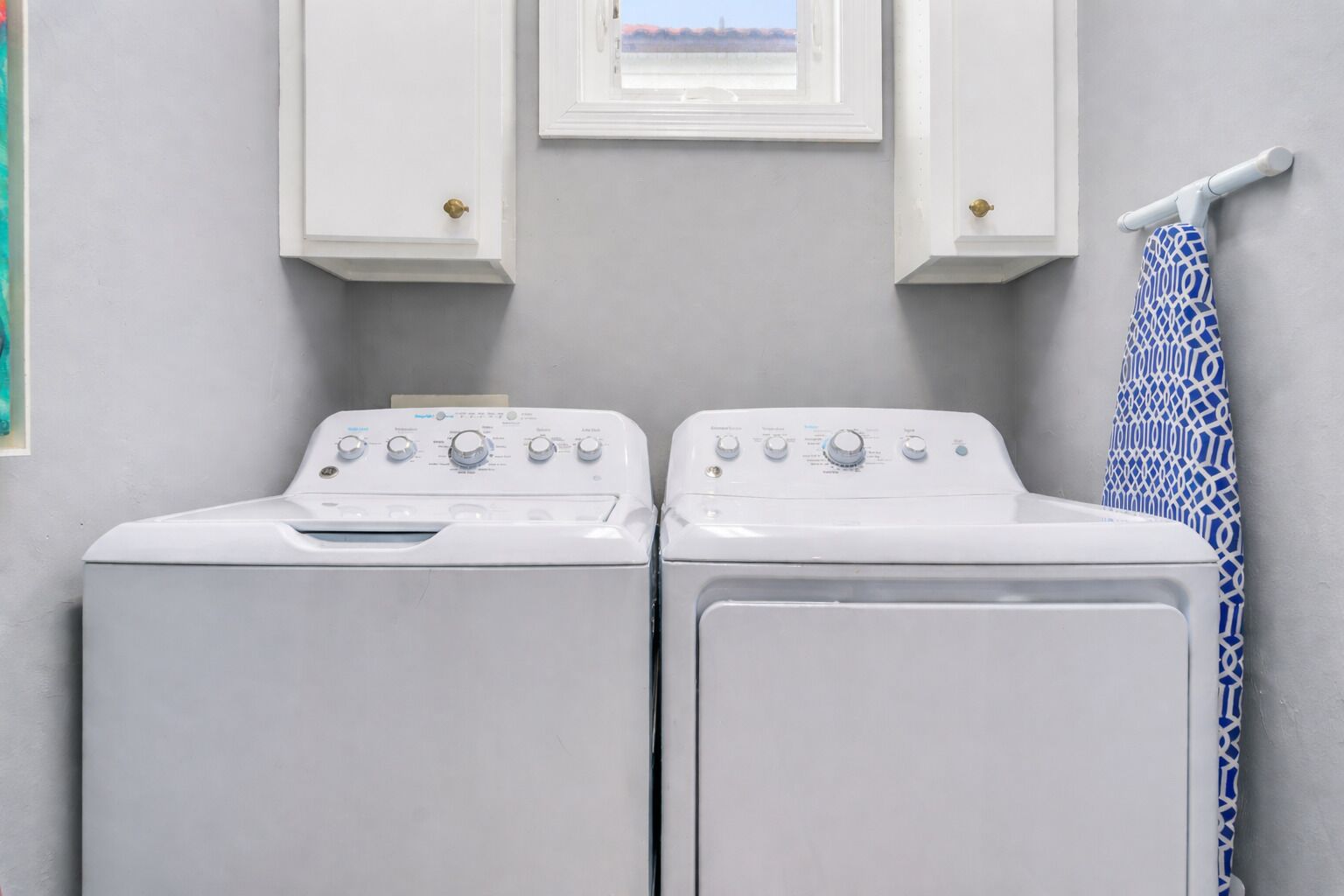 A laundry room with two white washing machines, a window above them, and a towel rack with a patterned towel.
