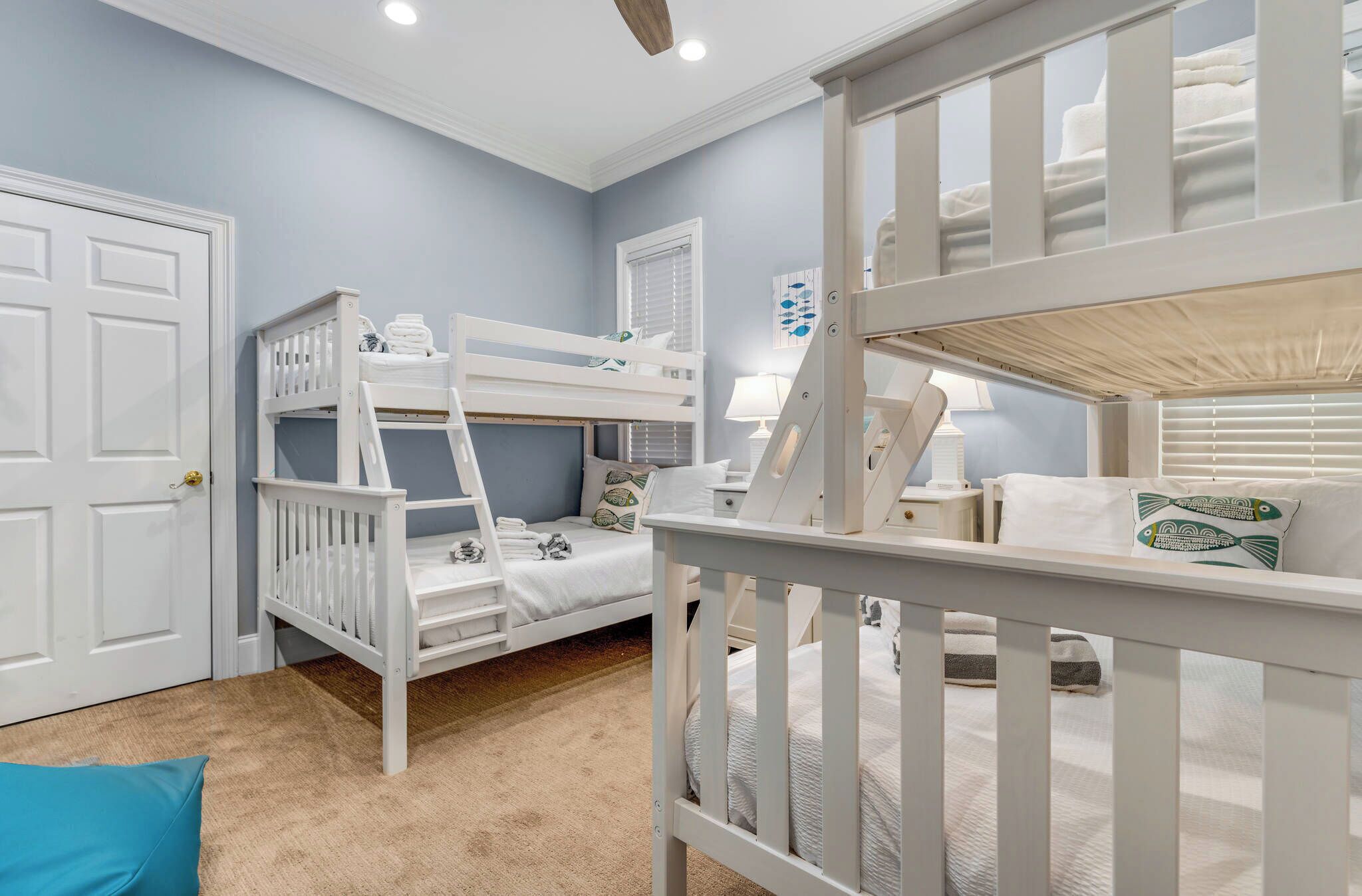 A room with bunk beds, a door, a lamp, and a window with blinds.