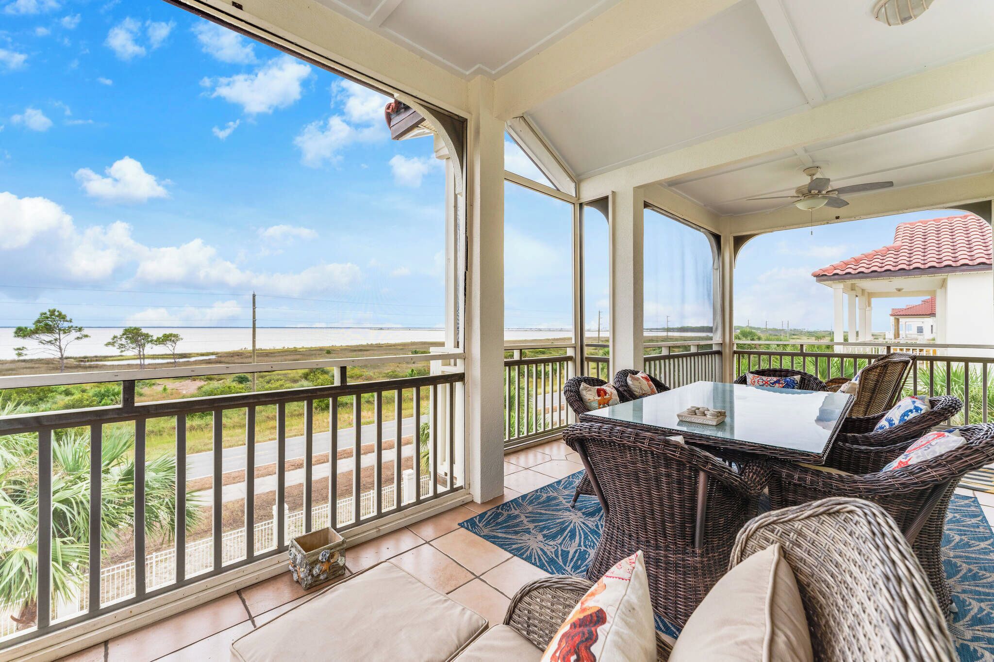 A covered outdoor area with a table and chairs, a view of the landscape, and a ceiling fan.