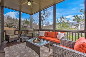 A covered outdoor seating area with wicker furniture, a glass coffee table, and a view of a residential neighborhood. - Paws Awhile - Mountain Vistas, Cozy Fireplace Chats, Movie Nights & Golf Swings (Jasper)