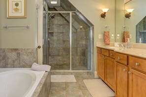 A bathroom with a glass shower enclosure, a bathtub, wooden cabinets, and a large mirror. - Paws Awhile - Mountain Vistas, Cozy Fireplace Chats, Movie Nights & Golf Swings (Jasper)