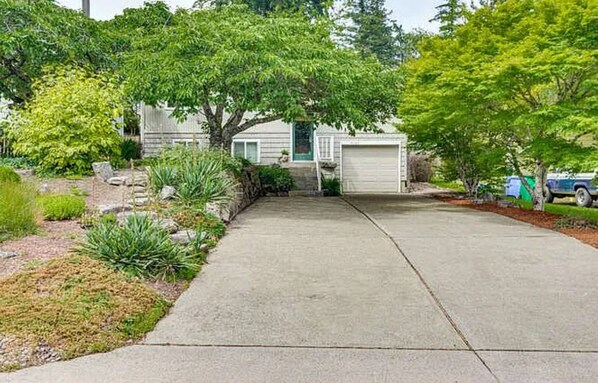 A residential driveway leading to a house with a garage, surrounded by greenery and a parked car. - The Getaway Base (Portland)