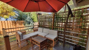 Una terraza de madera con una sombrilla roja, un banco de madera y una mesa de madera.