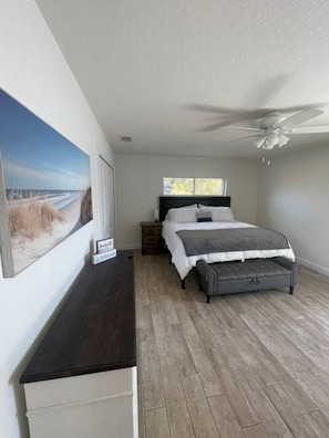 A bedroom with a bed, a nightstand, a dresser, a ceiling fan, and a large window. - Lakefront Pool Retreat • Theater 7.1 • Fishing (Lake Wales)