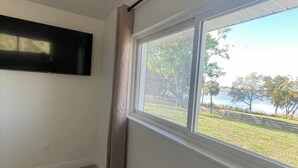A room with a large window, a flat-screen TV mounted on the wall, and a wooden floor.