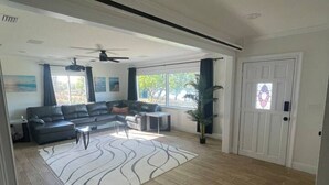 A spacious living room with a large window, a ceiling fan, and a patterned rug.