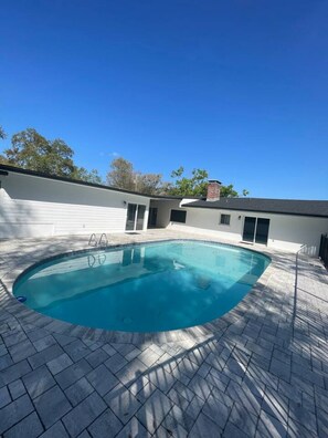 A swimming pool with a tiled deck, a small building with a door, and trees in the background. - Lakefront Pool Retreat • Theater 7.1 • Fishing (Lake Wales)