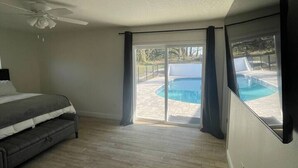 A bedroom with a bed, a ceiling fan, and a view of a swimming pool.