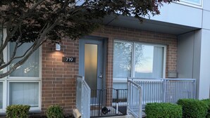 A two-story building with a brick facade, a numbered door, and a small porch with a metal railing. - Cozy 1-bedroom condo in serene Kansas City with AC and gym (Kansas City)