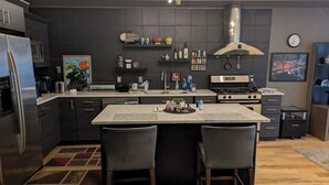 A modern kitchen with a central island, stainless steel appliances, and a variety of kitchen tools and appliances. - Cozy 1-bedroom condo in serene Kansas City with AC and gym (Kansas City)